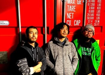 The three members of ZEROSHIKI standing against a red shipping container © ZEROSHIKI
