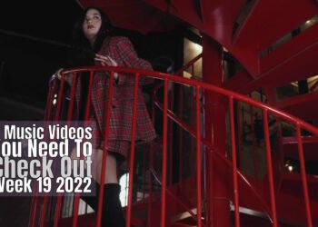 Still from LINO LEIA's music video for "ランテルディ (L’INTERDIT)". The musician is standing on a red-coloured staircase, apparently a fire escape. She is searching for something.