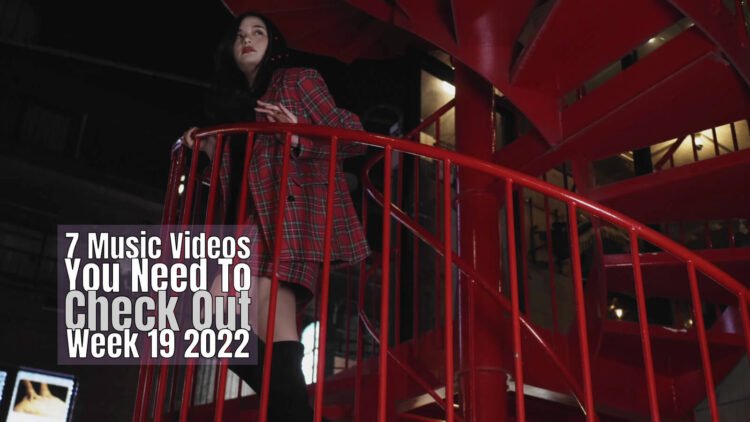 Still from LINO LEIA's music video for "ランテルディ (L’INTERDIT)". The musician is standing on a red-coloured staircase, apparently a fire escape. She is searching for something.