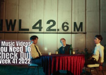 Still from Bob Paulsen's music video for "Doggs". The three band members of the rock band are sitting at a table at a seemingly outside location, waiting for their dinner.