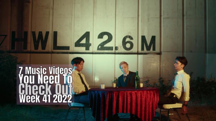 Still from Bob Paulsen's music video for "Doggs". The three band members of the rock band are sitting at a table at a seemingly outside location, waiting for their dinner.