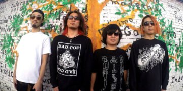 The photo shows the four members of STONE LEEK standing in front of a wall covered with graffiti. The graffiti includes a tree with green leaves and (Spanish) words. Three of the members wear black (sweat) shirts and one wears a white shirt.
