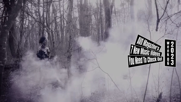 Still from HOWL's music video for "アンダーテイカー (Undertaker)". Vocalist Mayoi is walking through a partly misty forest, while dressed in dark clothing and wearing a beret. The colouring of this still is monochrome.