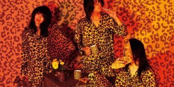 The three members of Boris dressed in panter print pyjamas are posing like people who just woke up after a good sleep, it includes a breakfast table that has a panter print cloth. They are surrounded by panter print as well.