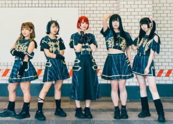 The five members of idol group DEMO, they are standing next to each other while posing and looking to the person who took the photo. They are dressed in feminine clothing with blue and green stripes, black patches and golden coloured embellishments and black coloured sneakers.