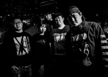 A monochrome band photo taken during the nighttime of Kruelty. The five members are seemingly dressed in dark-coloured clothing and are standing near each other and looking into the camera lens.