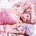 Nana Kitade is dressed in pink clothing and posing while lying on pillows and blankets. © BABYLONIA LLC