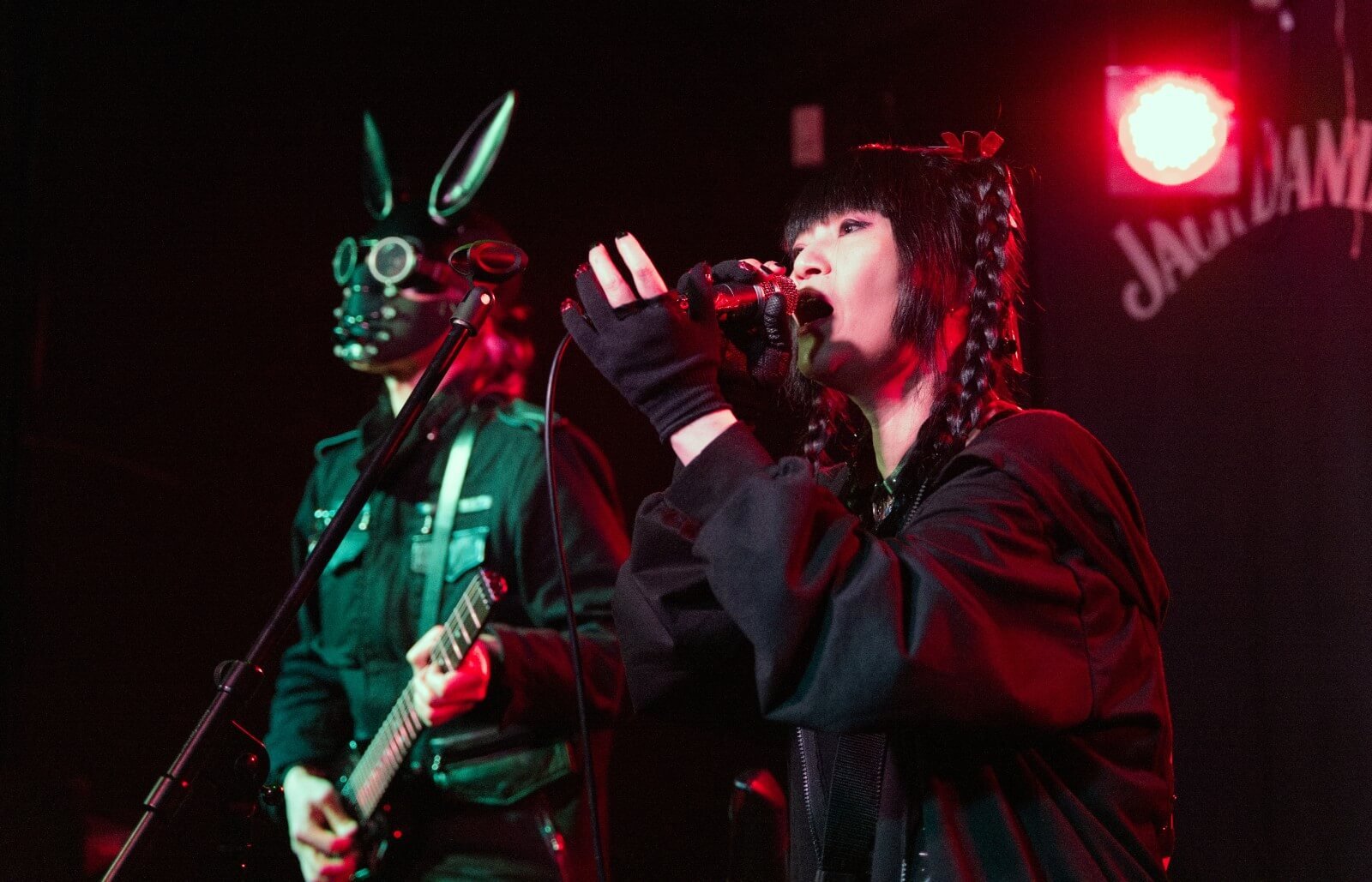 PSYDOLL at The Sunflower Lounge (Birmingham). Both members are dressed in dark clothes. One of the members of PSYDOLL is wearing a maks with seemingly bunny ears and plays the guitar, while the other member is singing. | Photography by James Grant (wonderlens)