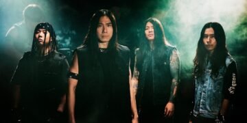 The four members of Sable Hills, dressed in dark clothes, pose in front of an apparent audience, lights are shone on them from behind so that they are very clear in the picture. © SABLE HILLS