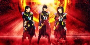 The three members of BABYMETAL are posing while being surrounded of what looks like fire.