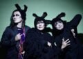 The three members of cali≠gari are standing next to each other. They are dressed in mostly dark clothing, wearing dark eye makeup and wearing headgear resembling fluffy bunny ears. © cali≠gari