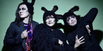 The three members of cali≠gari are standing next to each other. They are dressed in mostly dark clothing, wearing dark eye makeup and wearing headgear resembling fluffy bunny ears. © cali≠gari