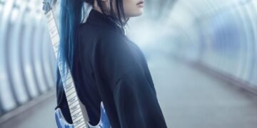 Band leader Kai is dressed in black clothing and carries a soft blue-coloured electric guitar on the back. Kai seems to be walking on an empty train station or in an empty tunnel and looks behind him.