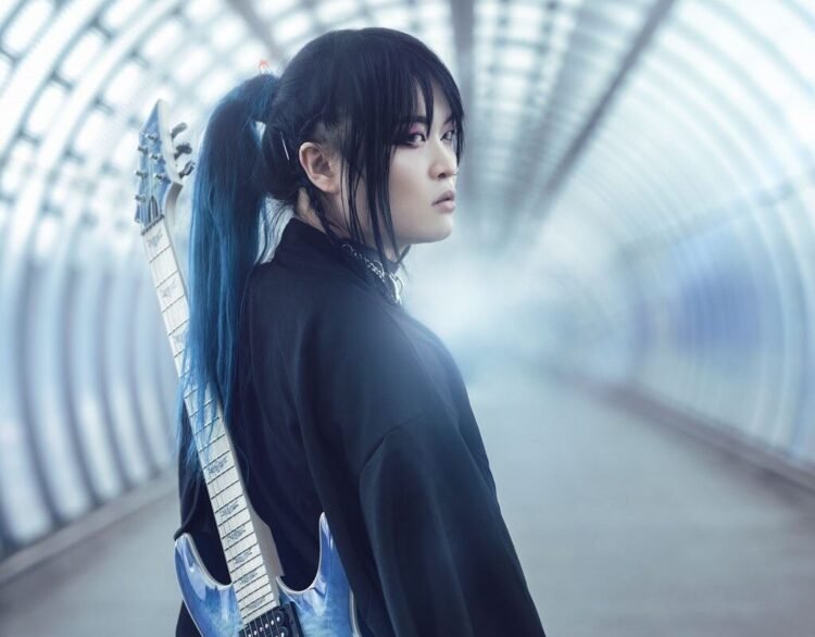 Band leader Kai is dressed in black clothing and carries a soft blue-coloured electric guitar on the back. Kai seems to be walking on an empty train station or in an empty tunnel and looks behind him.
