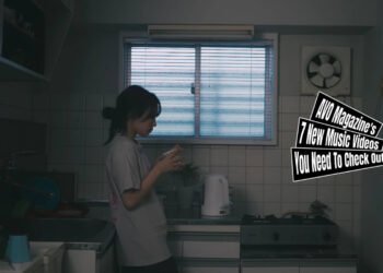 Still from the music video by the band ミイ (Myy) for the song "失恋 (Shitsukoi)". A girl with a ponytail in a lose knot is standing in lightly dim kitchen. There are some cleaned dishes air drying, while the girl is drinking from a cup. In the still it looks like she is deep in thoughts.