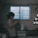 Still from the music video by the band ミイ (Myy) for the song "失恋 (Shitsukoi)". A girl with a ponytail in a lose knot is standing in lightly dim kitchen. There are some cleaned dishes air drying, while the girl is drinking from a cup. In the still it looks like she is deep in thoughts.
