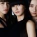 Group photo of Perfume, the three members are dressed in dark clothes and stand very close together.