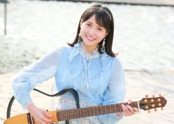 MION in a blue dress holds her signature electric guitar. © MION