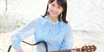 MION in a blue dress holds her signature electric guitar. © MION