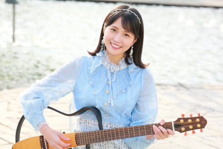 MION in a blue dress holds her signature electric guitar. © MION
