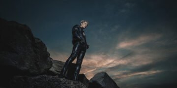 Miyavi dressed in black leather is standing on a rock formation.