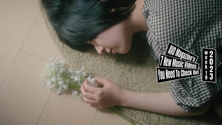 Still from a music video by ステエションズ (Stations) for the song "LOVE". A girl with black hair is lying on a round carpet and looks at a small bouquet of flowers.