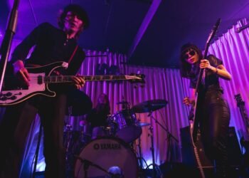 An action photo of The Highmarts on stage with bassist Atsushi in front and guitarist and vocalist Suzu and drummer Minako in the background. The photo was taken in March 2023, during a show organised by the band itself at Shimokitazawa Live Haus.