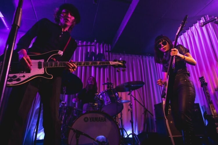 An action photo of The Highmarts on stage with bassist Atsushi in front and guitarist and vocalist Suzu and drummer Minako in the background. The photo was taken in March 2023, during a show organised by the band itself at Shimokitazawa Live Haus.
