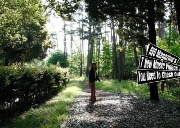 Still from quorca's music video for their first release "ターコイズ (Turquoise)". A girl, walking on a path in a forest where the leaves allow the sunlight in little by little, turns around.
