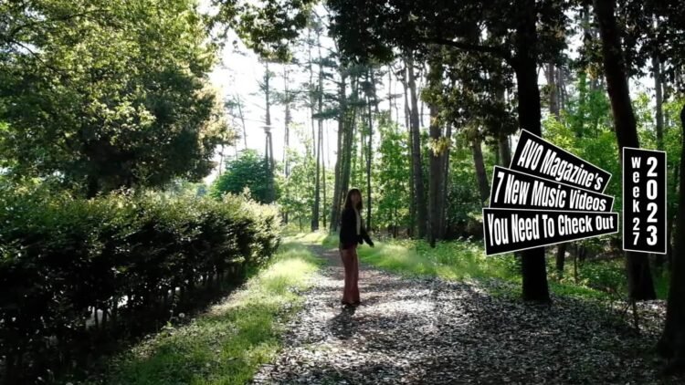Still from quorca's music video for their first release "ターコイズ (Turquoise)". A girl, walking on a path in a forest where the leaves allow the sunlight in little by little, turns around.