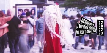 Still from Kako Fujita's music video for the song "怪物 (Kaibutsu)". A woman with a special costume - made by Emi Fukumoto - consisting of a red dress and a white-coloured artsy headpiece stands in the middle of a busy pedestrian crossing.