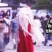 Still from Kako Fujita's music video for the song "怪物 (Kaibutsu)". A woman with a special costume - made by Emi Fukumoto - consisting of a red dress and a white-coloured artsy headpiece stands in the middle of a busy pedestrian crossing.