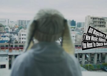 Still from SOM4LI's music video for the song "メイ (Mei)". A person is wearing a bunny hat and looks out from the balcony to the city and public transport.