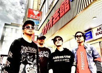 The four men of Satsuriku Robot are standing in front of a building, posing for the camera. They are wearing band shirts or hoodies in mostly dark colours. In addition, they are all wearing sunglasses.