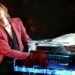 This photo captures an intimate moment between the musician YOSHIKI and Kawai piano on stage. He wears a red jacket and black blouse.YOSHIKI has his eyes closed and appears to be deeply focused on his music.