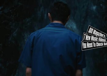 Still from CANDYGIRL's music video for "WATERFALL". A man with a blue shirt is standing in front of a waterfall. In the still, the back of the man is shown.