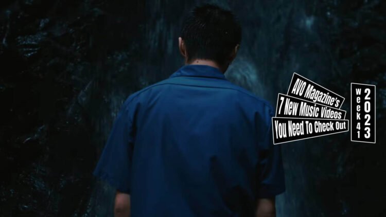 Still from CANDYGIRL's music video for "WATERFALL". A man with a blue shirt is standing in front of a waterfall. In the still, the back of the man is shown.