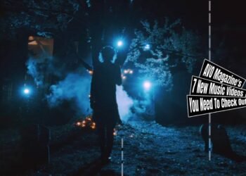 Still from the music video "ジャック・オ・ドキドキ (Jack’o’doki-doki)" by the band グラビティ (Gravity). The vocalist of Gravity is standing in the dark on a location that looks like a small graveyard with a few gravestones and a tree. There are some lights making the silhouette of the musician quite clearly, at the same time, it creates a little creepy atmosphere.