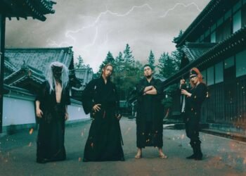 RYUJIN © Napalm Records - Four band members of the band RYUJIN are dressed in traditional Japanese clothing, hakama, their look is inspired by samurai, especially with the addition of the swords, and one of them has an oni mask on. All members are facing forward and surrounded by old Japanese buildings. The dominant colours in this photo are dark; black and green-greyish. The sky is dark and cloudy, illumminated by flashes of lighting. The scene has an air of mystery about it, but is placed in Japan giving an extra touch to the traditional vibe.