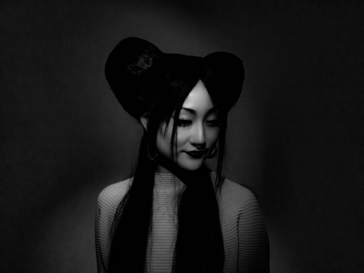 A monochrome close-up of Hinako Omori with two big buns in her hair but also has part of her hair loose. She wears a striped shirt and does not look into the camera but looks sideways down with a soft smile.