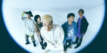 Band photo of the five-piece coldrain made with what seems a fisheye lens. The band members are standing next to each other, some band members look away, the vocalist Masato, who stands in the middle, leans forward towards the camera lens. Photo by Yao Lange