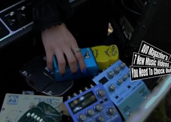 Still from the music video "Insane Supermarket" by the band CIGARETTE in your bed. The image features a person's hand that places a guitar pedal in a supermarket cart filled with other musical equipment, including an amplifier, other guitar pedals and other equipment. The cart stands in the middle of a forest.