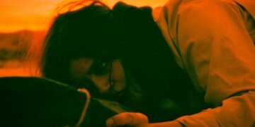 The young lady in the film “Live Pilgrimage in Madrid” lies on the ground and looks intensely to a certain object that she holds in her left hand. - Still "Live Pilgrimage in Madrid" | MONO, ALISON