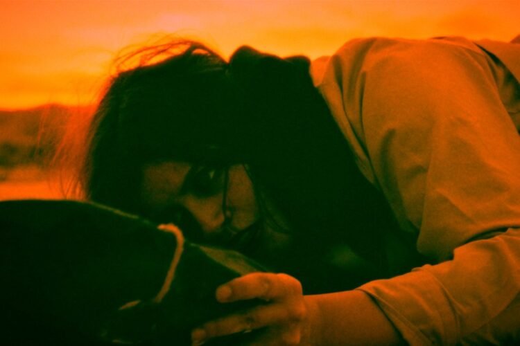 The young lady in the film “Live Pilgrimage in Madrid” lies on the ground and looks intensely to a certain object that she holds in her left hand. - Still "Live Pilgrimage in Madrid" | MONO, ALISON
