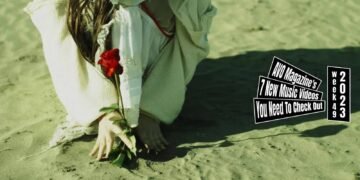 Still from the music video "scream" by the band ペッテルズ (Pettels). The vocalist and guitarist of Pettels is at a beach and is dressed in a white dress and a cardigan, and plants a red rose into the ground. The still is mirrored.