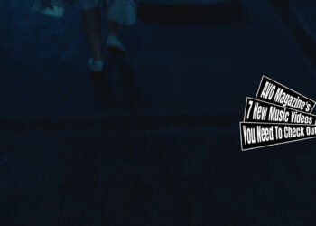 Still from the music video for "Hameln" by the band 灰かぶり (The Cinder). The still shows one of the dancers in the music video wearing white shoes and a white dress with colourful marks made by paint as she walks away from the screen and the camera is pointed at the floor. The surroundings of this location looks very dark.