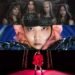 The image is a collage composed of three promotional photos from the artists SARI, ERISU and NEMLESSS. The four members of ERISU are posing in a dark location clothed in dark ritualistic clothing. SARI in a black top with a black and pink hat on her head and black gloves. According to SARI, this is outfit has an octopus concept. NEMLESS is dressed in a red outfit wiht a cape, standing on what seems like a red stage with behind her a neon version of a tori.