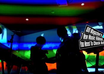 Still from the music video by 導天和 (Dao Teng Hou) for the song "龍頭蛇尾 (Dragon Head, Snake Tail)". The image features the band 導天和 (Dao Teng Hou) performing against a vibrant and colourful background with a rainbow gradient. Because of the lighting behind them, the three musicians can't be seen well and thus in the dark.
