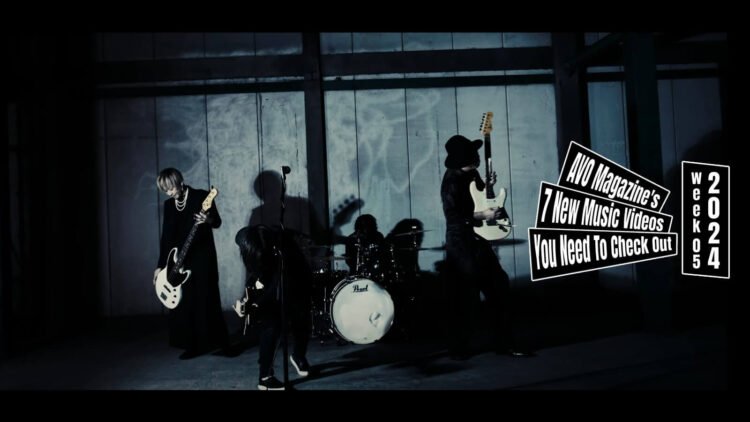 Still from the music video "アリガトウ (Arigatou)" by the band Luin. The still depicts the band Luin performing in a space with dim lighting making the atmosphere moody. The musicians, dressed in black, are playing various instruments including a bass guitar, the drums, and guitars.
