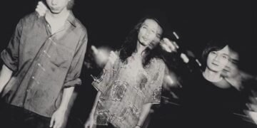 The monochrome photo of the three men of Dhidalah seems to be taken outside during nighttime. The photo has some blurring effect as if the musicians have moved a bit while the photo was taken or this is a combination of two photos. Photography by Kentaro Takahashi